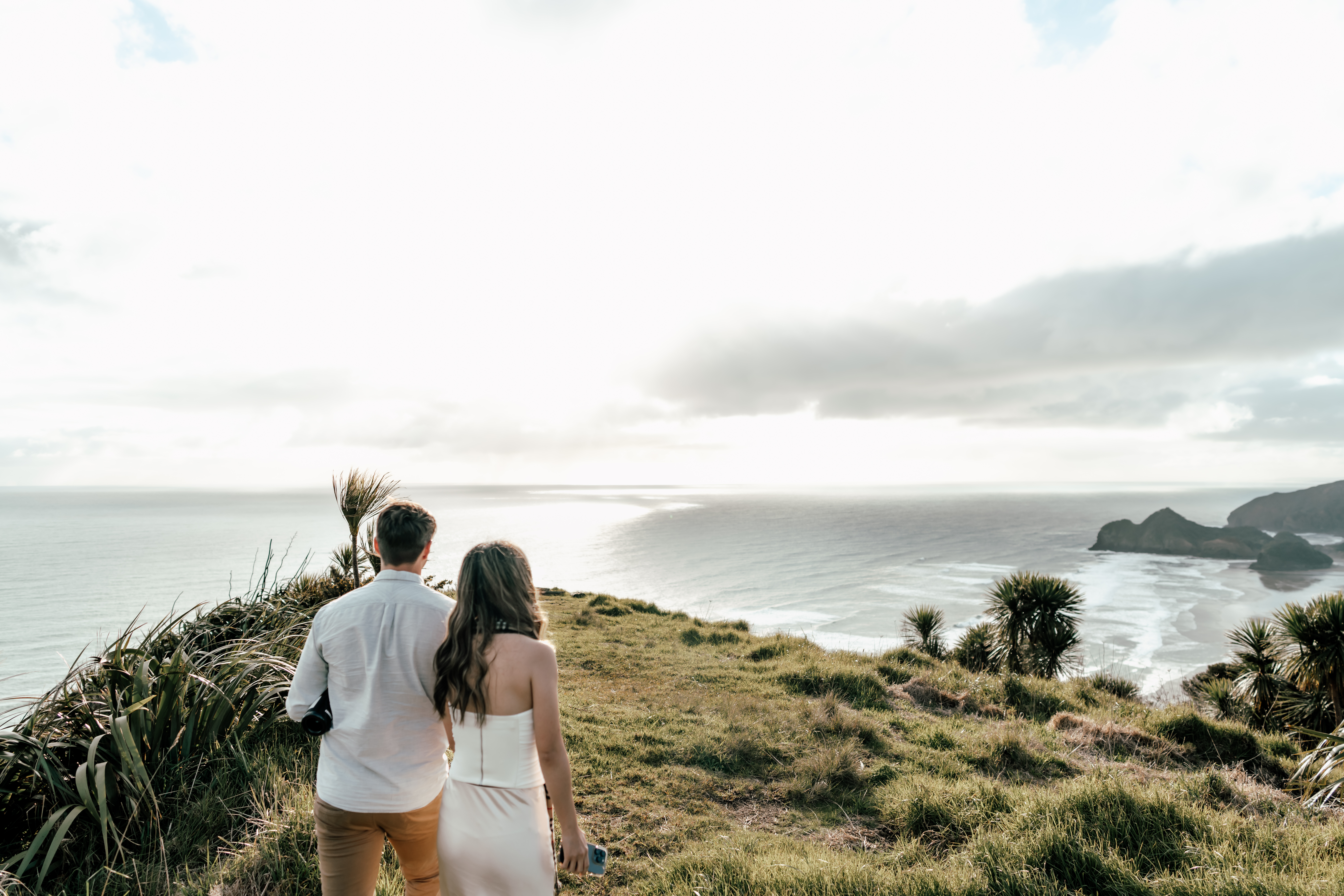 Couple walking towards the beautiful view after landing at Bethells beach by helicopter for their proposal