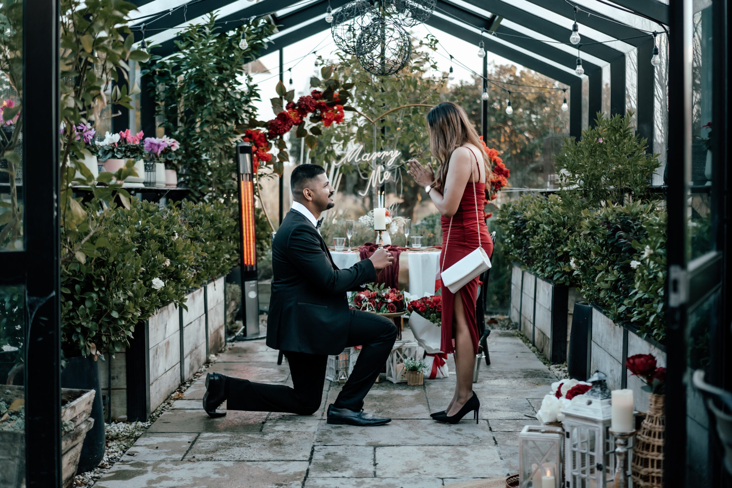 Romantic proposal at The Grange in Takapuna with red roses, candles, and elegant décor, as Krishant proposes to Dipanjali in a red gown and black suit.