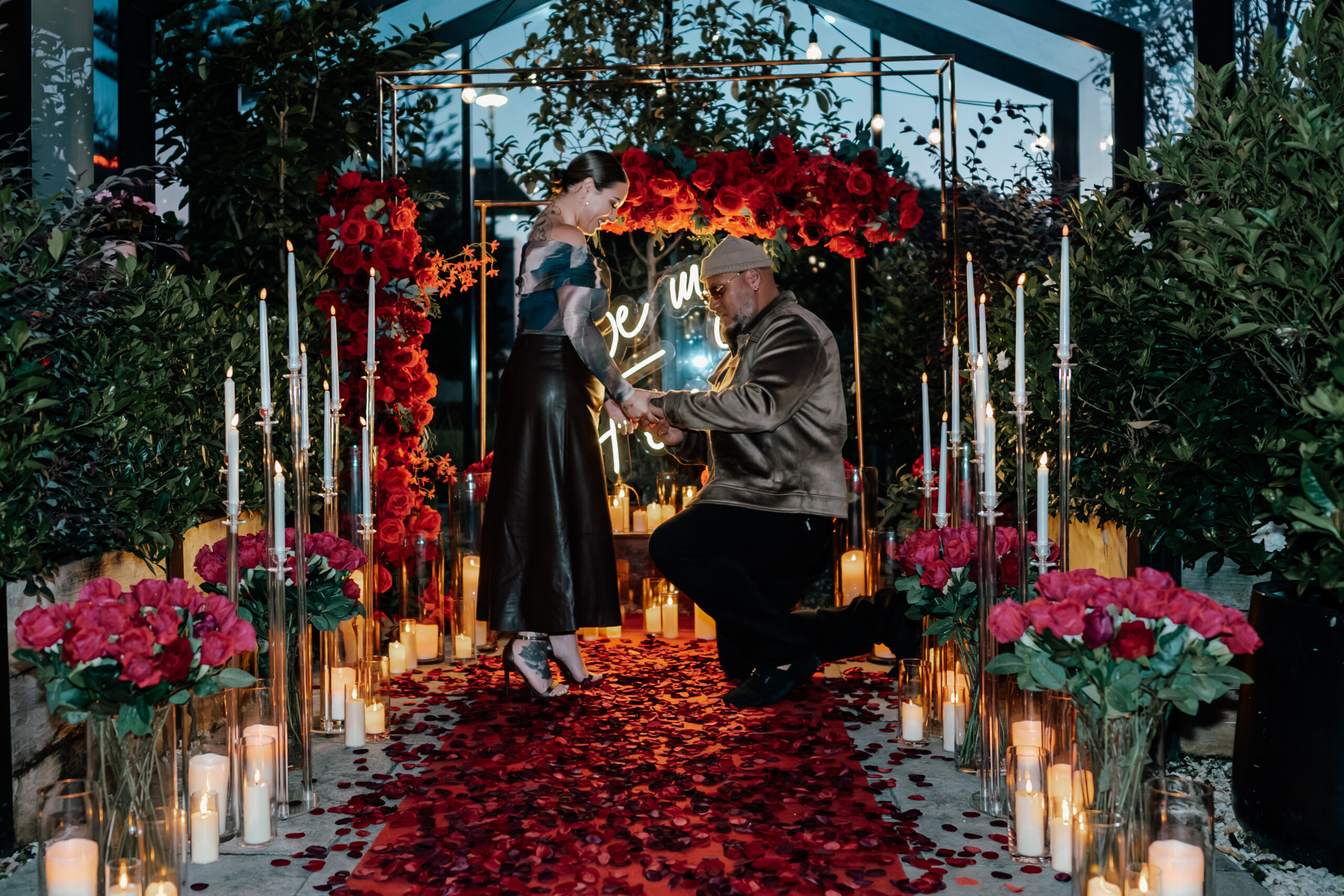 Romantic proposal at The Grange Takapuna Greenhouse with “Be My Forever” sign, lush plants, and emotional engagement moment